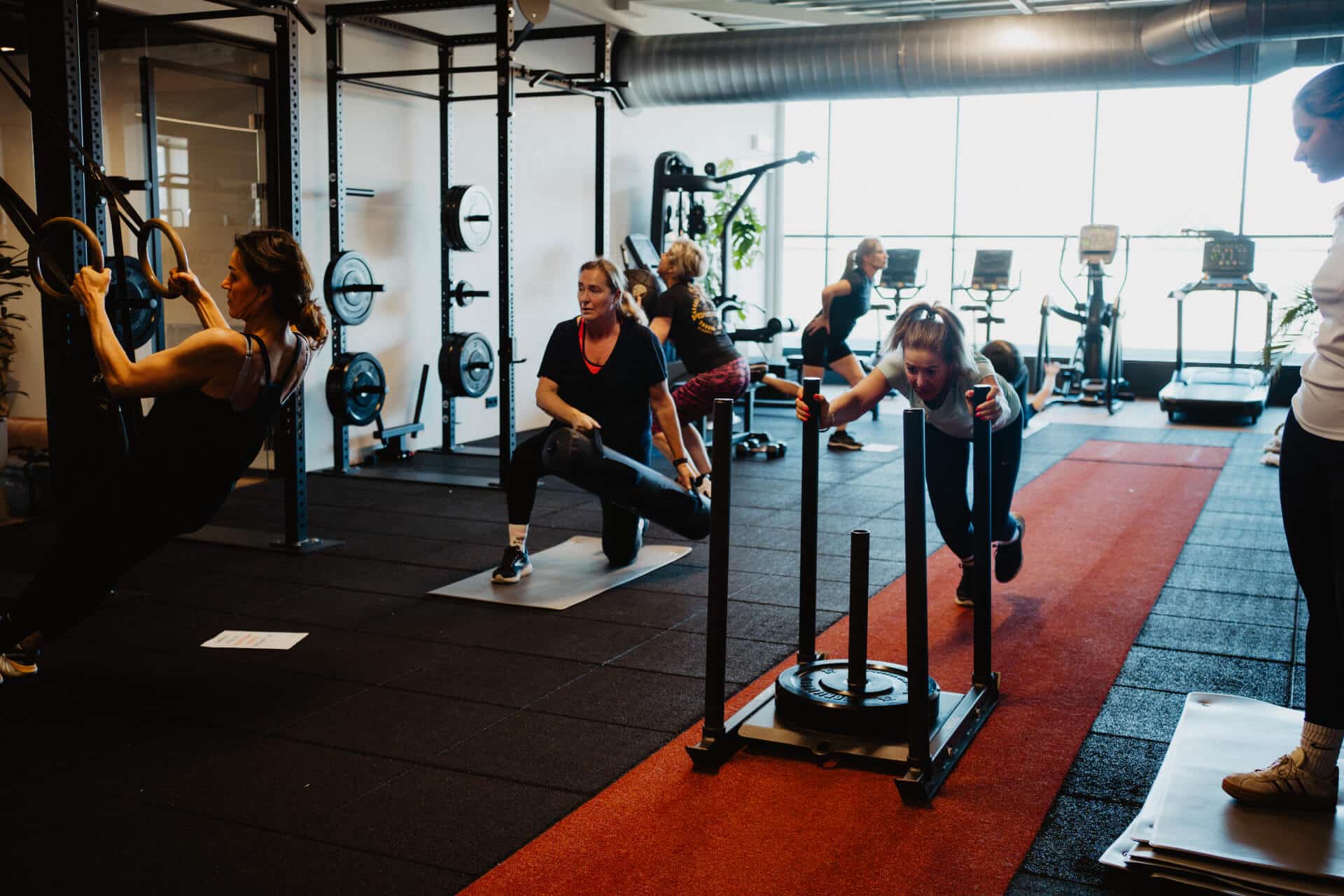 Groep sporters voert sled push en ring row oefeningen uit tijdens een Crossrox-les bij Peppergym.