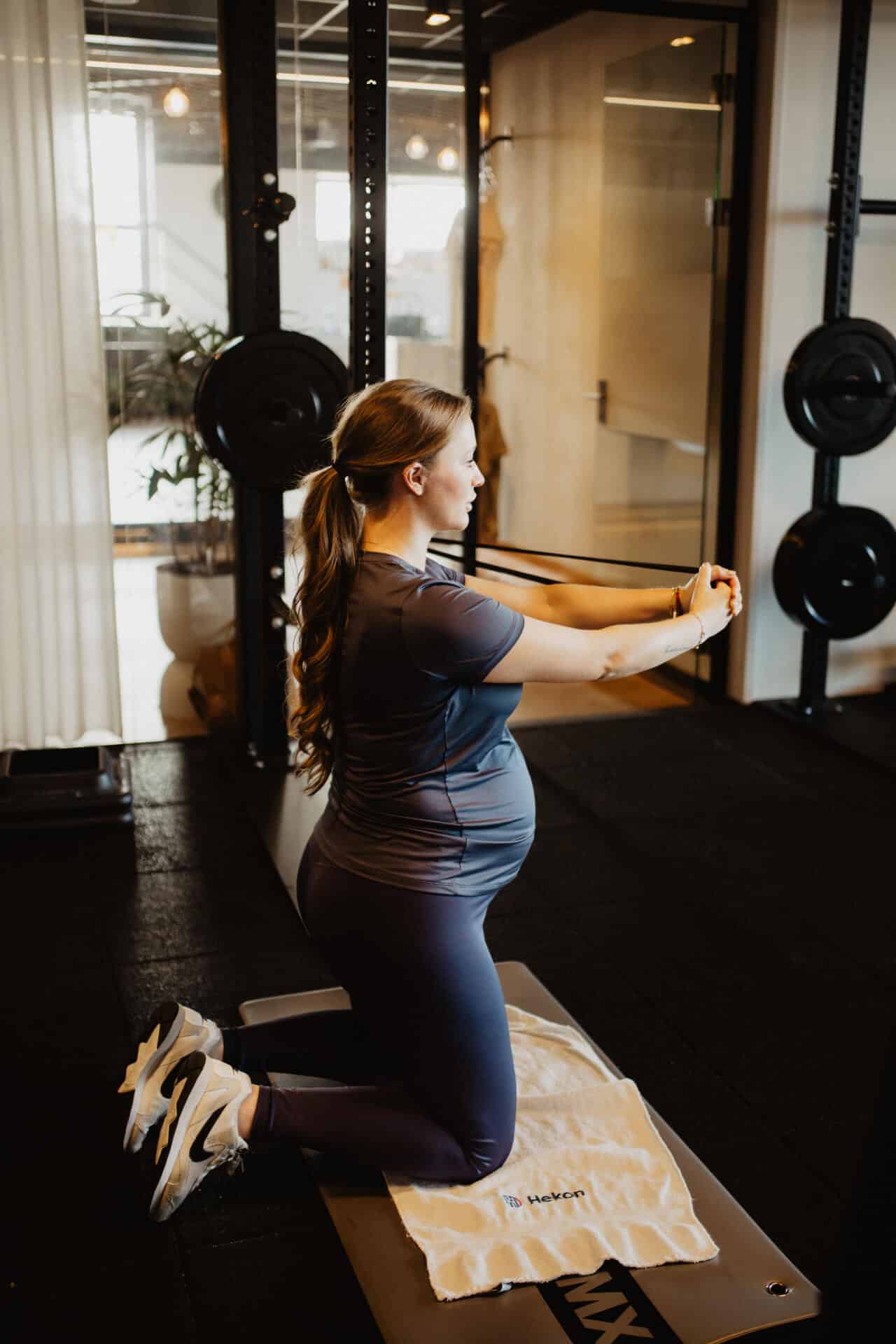 Zwangere vrouw doet een oefening met een weerstandsband op een mat bij Peppergym tijdens een Fitmama-les.