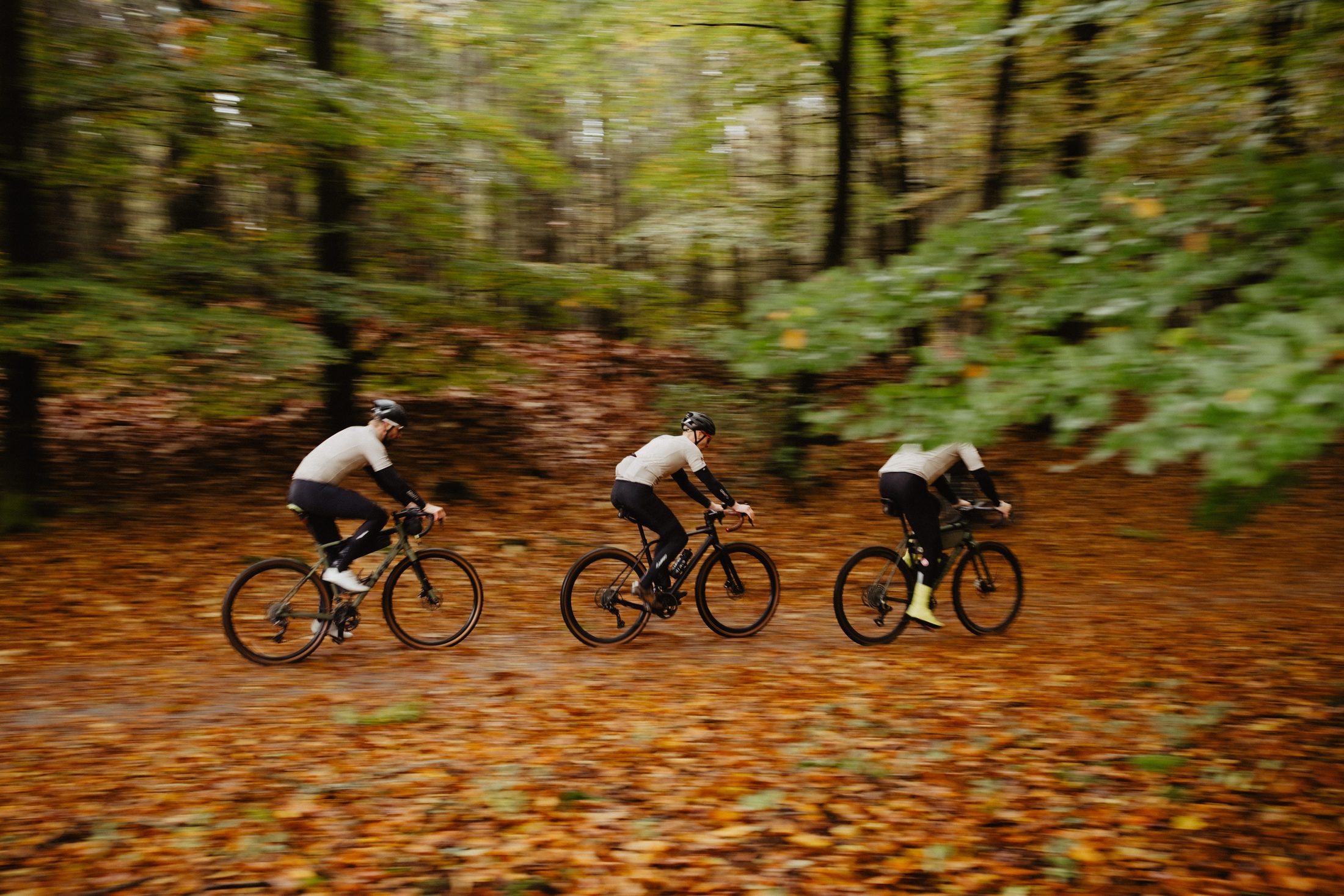 Drie gravelfietsers rijden over een bospad vol herfstbladeren