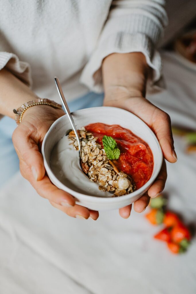 Handen houden een kom met granola, yoghurt en aardbeiencompote vast